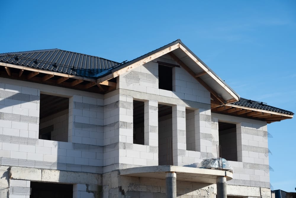 Bâtiment en construction avec des blocs de béton cellulaire et des tuiles de toit sous un ciel bleu, représentant le développement résidentiel et l’investissement immobilier.