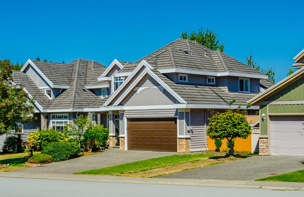 Grande maison de luxe sur mesure avec une cour avant joliment aménagée et taillée, ainsi qu’une allée menant au garage, située dans la banlieue de Vancouver, au Canada.
